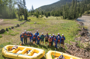 a group of people sitting on a raft in a forest with Wyoming River Trips in Cody Wyo. River trip facts and what to wear on your river trip.